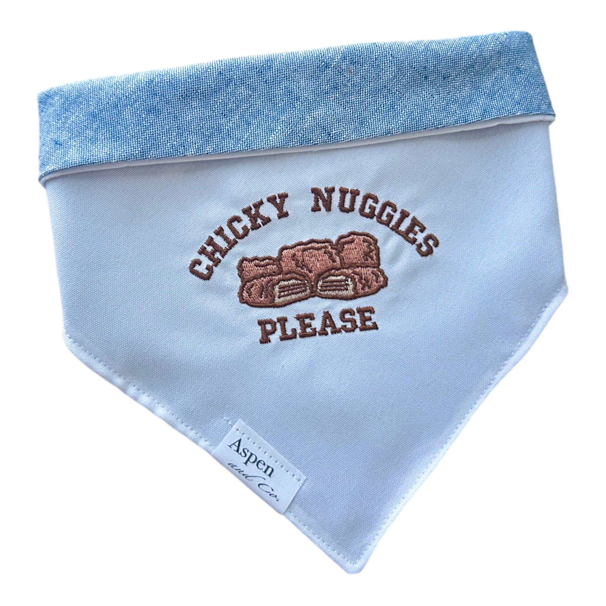 White embroidered dog bandana with the phrase “chicky nuggets please,” shown with blue linen backing for a stylish, reversible look.