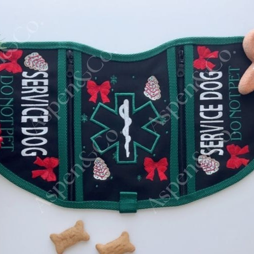 Black and green Christmas-themed service dog vest with cookie embroidery, medical alert symbol, and holiday text. Features two zippered pockets