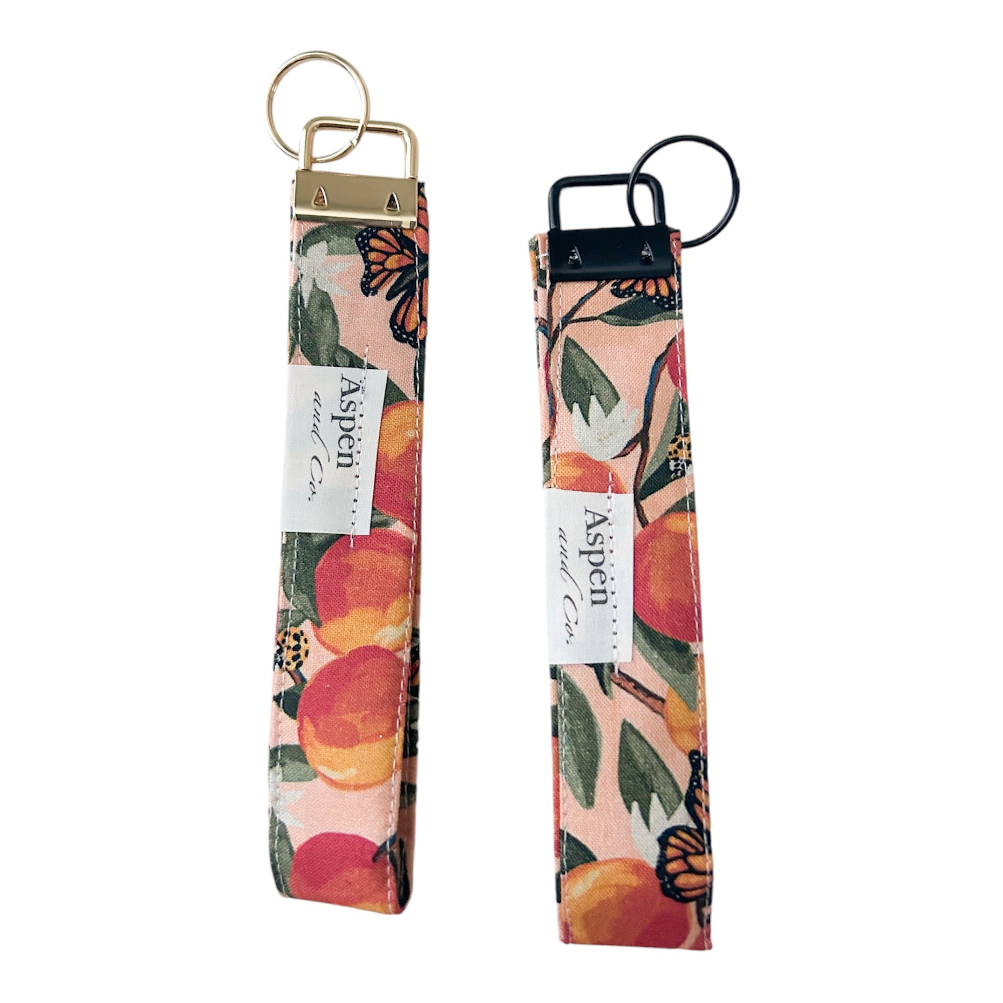 Back view of peach monarch butterfly key fob wristlets showing Aspen and Co tag with gold and black hardware options, durable cotton fabric, perfect for keys and IDs