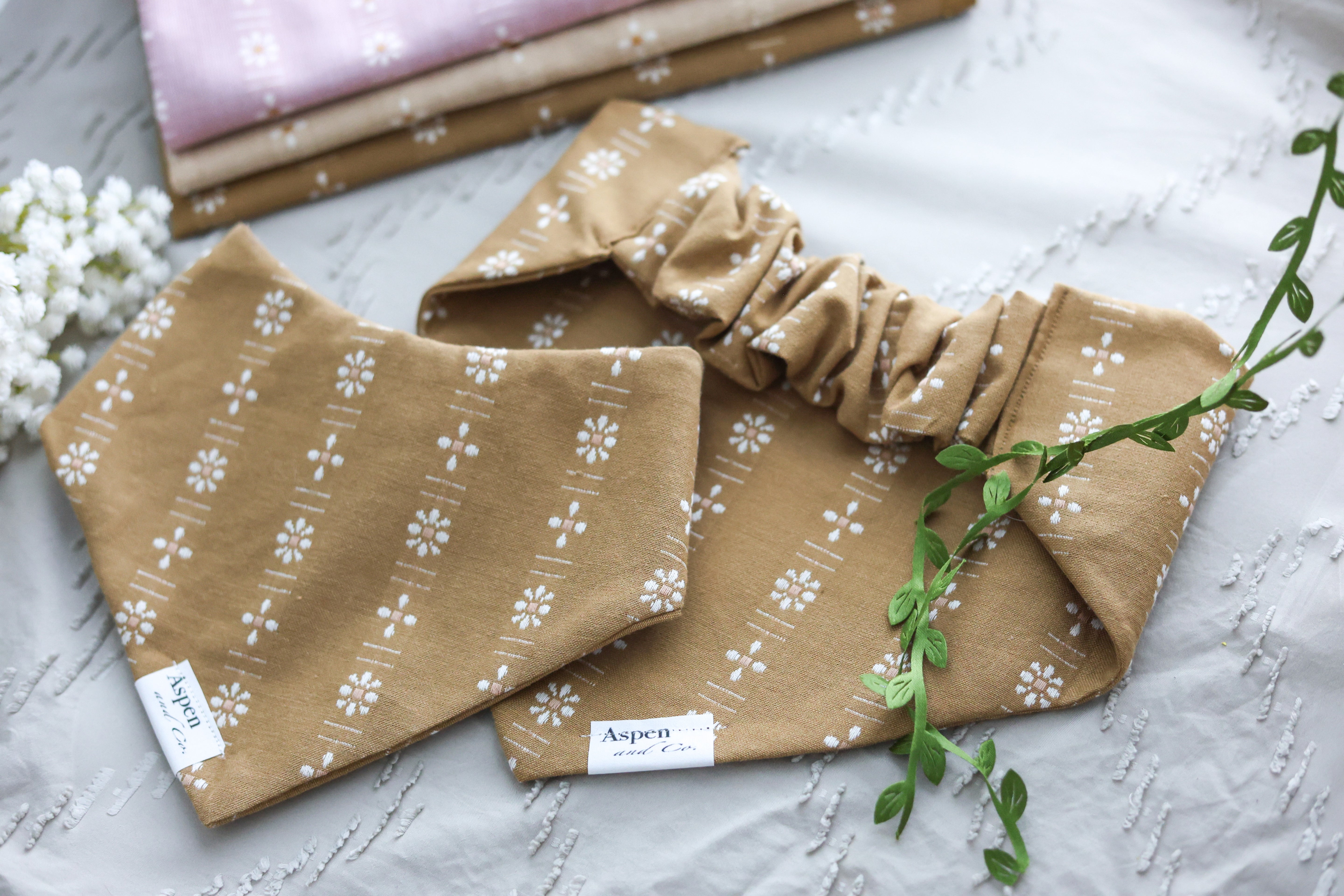 Ochre floral slip-on dog bandana shown front and back on sand colored background with white florals and additional woven fabric options