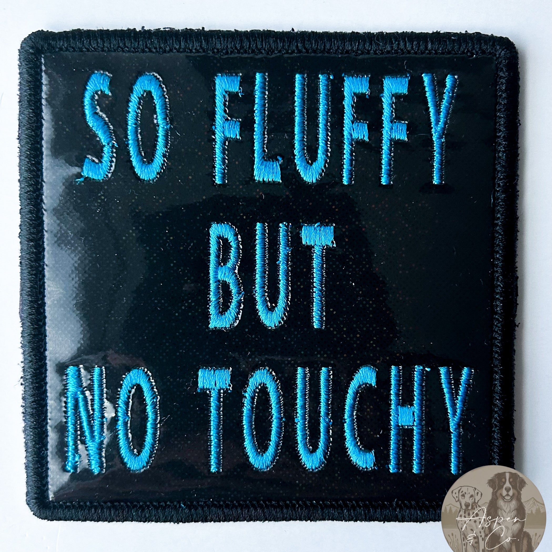 Black sparkles holographic embroidered dog patch with blue 'So Fluffy But No Touchy' text, designed for attaching to dog vests, harnesses, or capes.