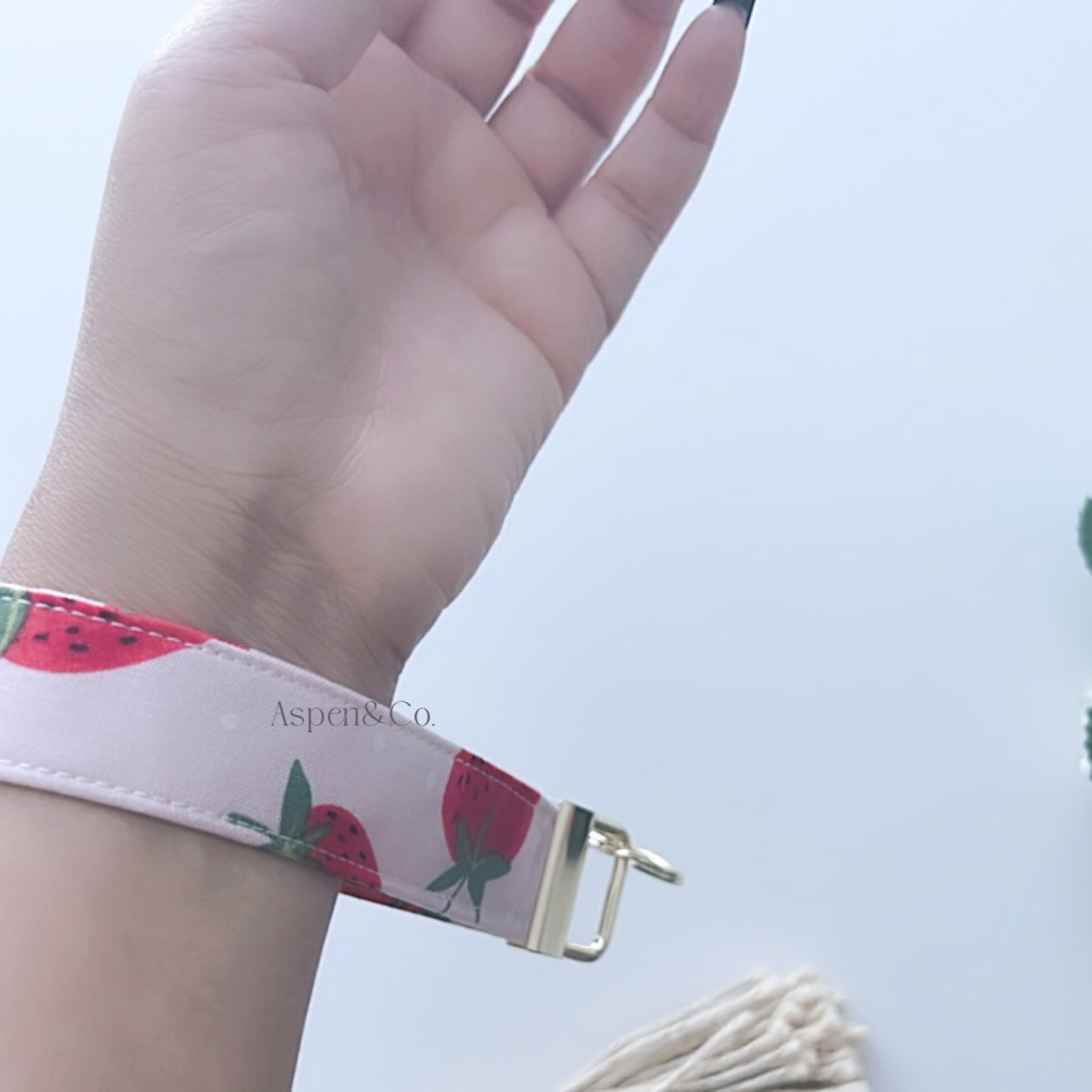 Hand wearing a floral keychain wristlet with decorative elements on a light background