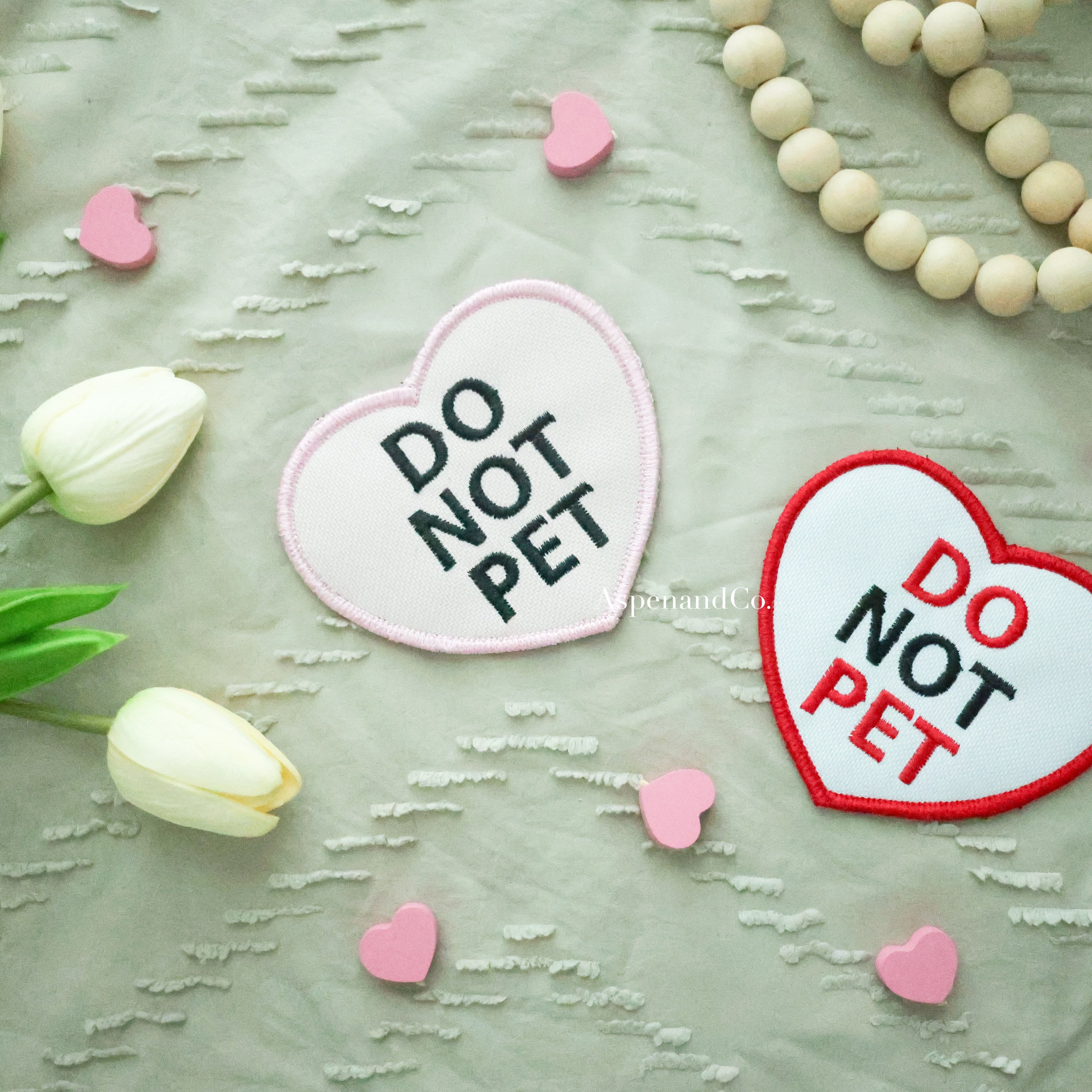 Side-by-side pink and white embroidered heart patches with 'DO NOT PET' text, designed for dog gear visibility
