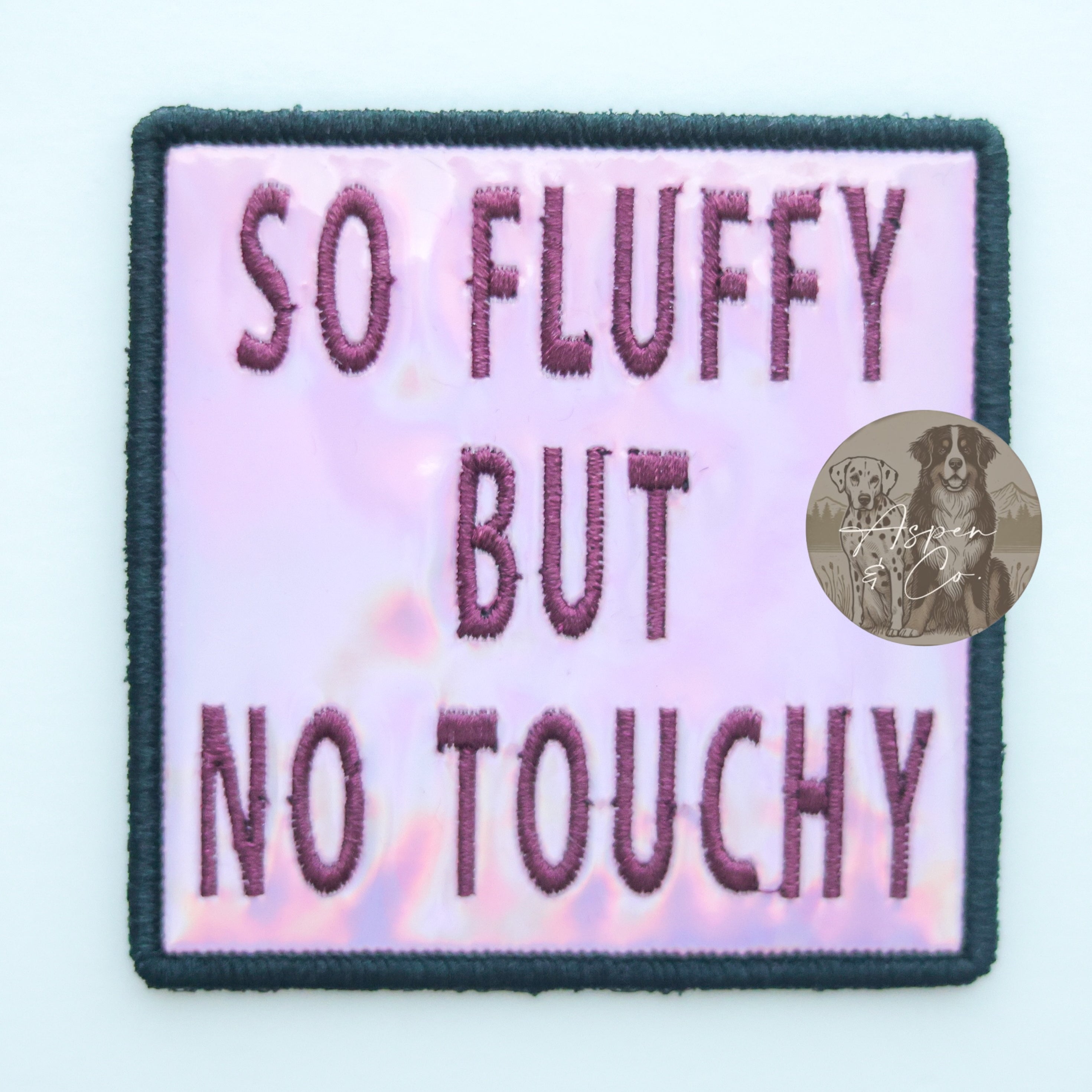 Pink holographic embroidered dog patch with plum 'So Fluffy But No Touchy' text, designed for attaching to dog vests, harnesses, or capes.