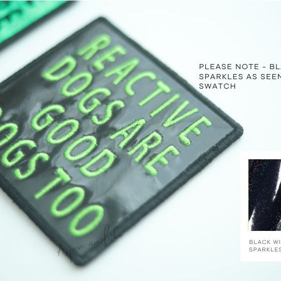 Close-up photo of a black holographic dog patch with neon green text reading "Reactive Dogs Are Good Dogs Too," designed for harnesses, vests, or capes.