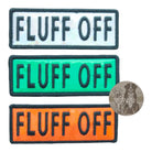 Photo showing silver, green, and orange holographic dog patches with the text "FLUFF OFF," designed for collars, harnesses, and vests.