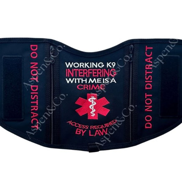 A black saddle-style service dog vest with bold red embroidery reading “WORKING K9 INTERFERING WITH ME IS A CRIME – ACCESS REQUIRED BY LAW,” flanked by “DO NOT DISTRACT” on both sides. Features two black 6x2" hook-and-loop patch panels. Made by Aspen & Co