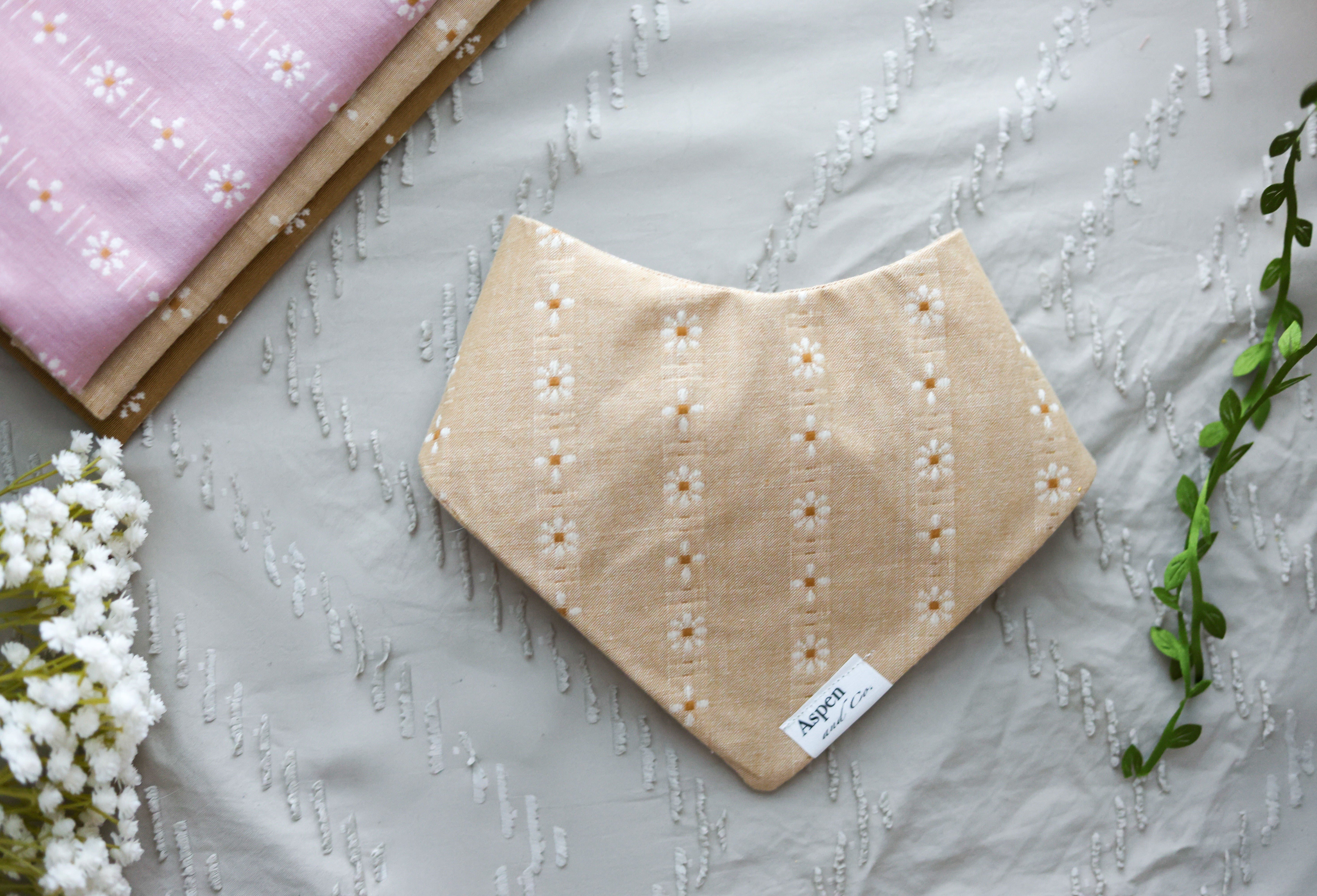 Single camel floral dog bandana shown from the front view, laid flat on sand with white flowers for styling.