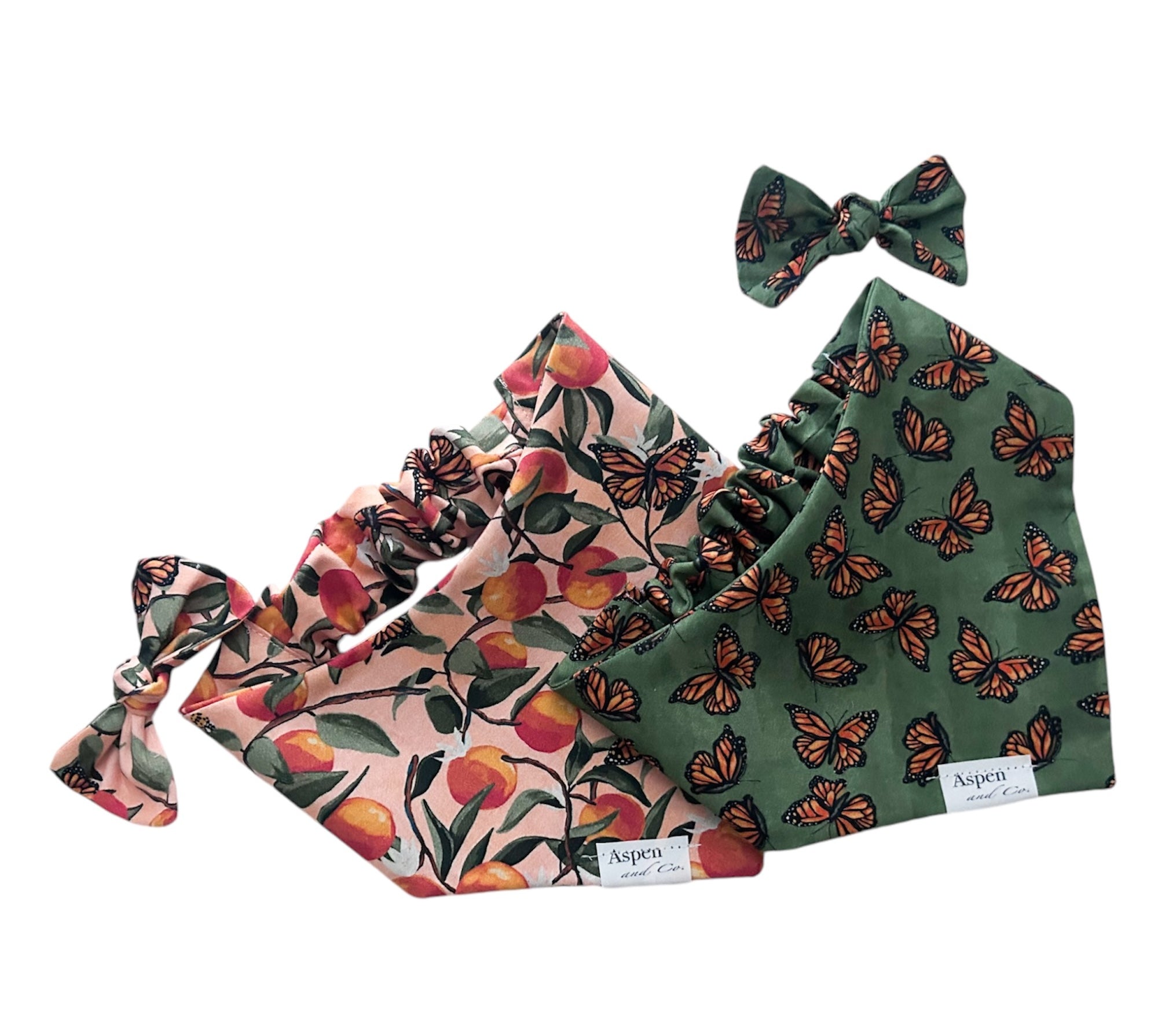 Photo showing two Monarch Butterfly scrunchie slide-on dog bandanas, both front side up—one in olive green and the other in peach—each featuring assorted monarch butterflies and a curved neckline. Both bandanas are double-layered and handmade.