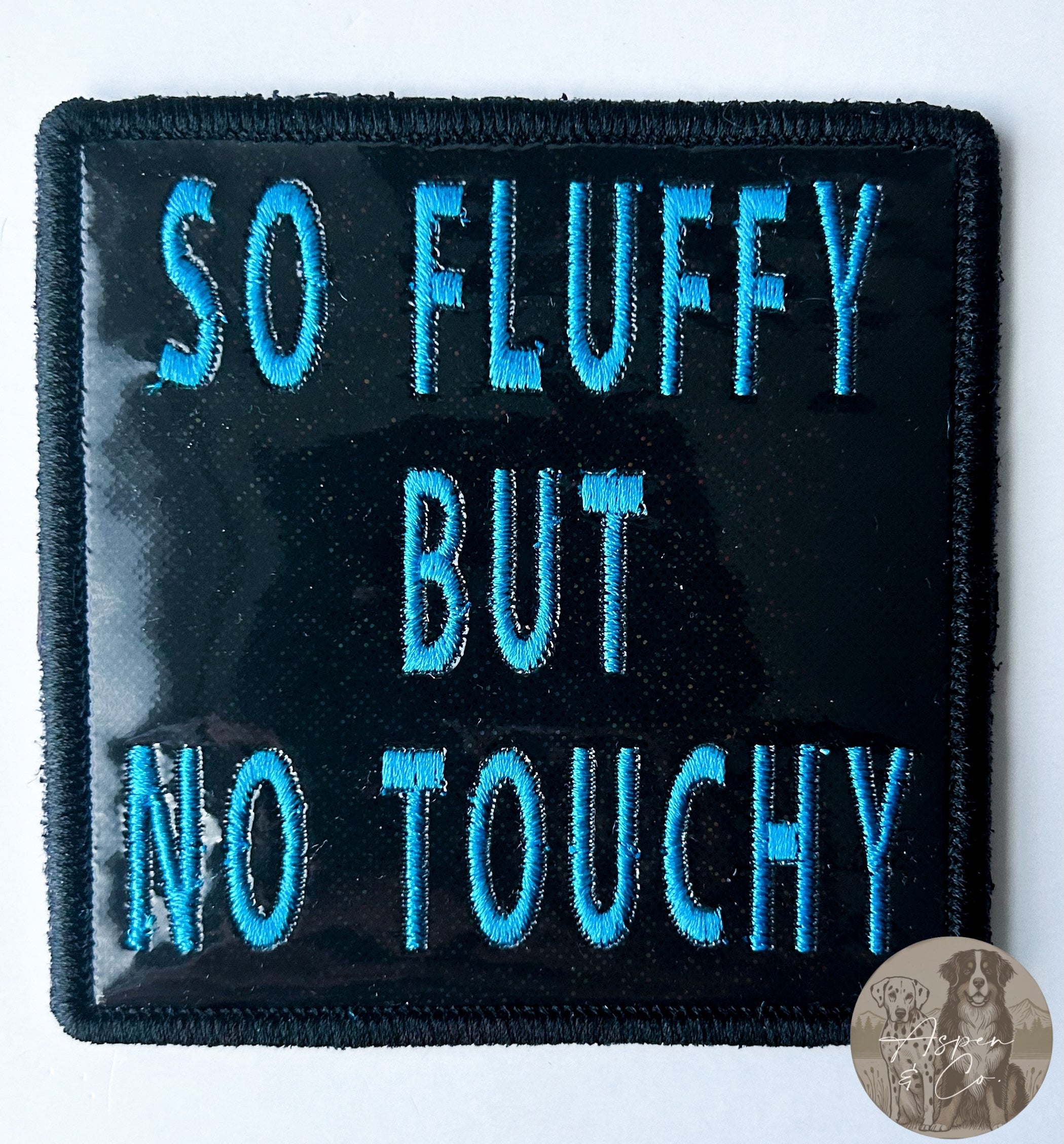 Black sparkles holographic embroidered dog patch with blue 'So Fluffy But No Touchy' text, designed for attaching to dog vests, harnesses, or capes.