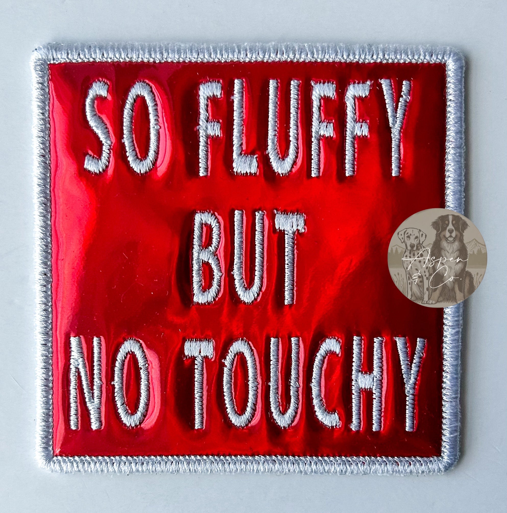 Red holographic embroidered dog patch with white 'So Fluffy But No Touchy' text, designed for attaching to dog vests, harnesses, or capes.