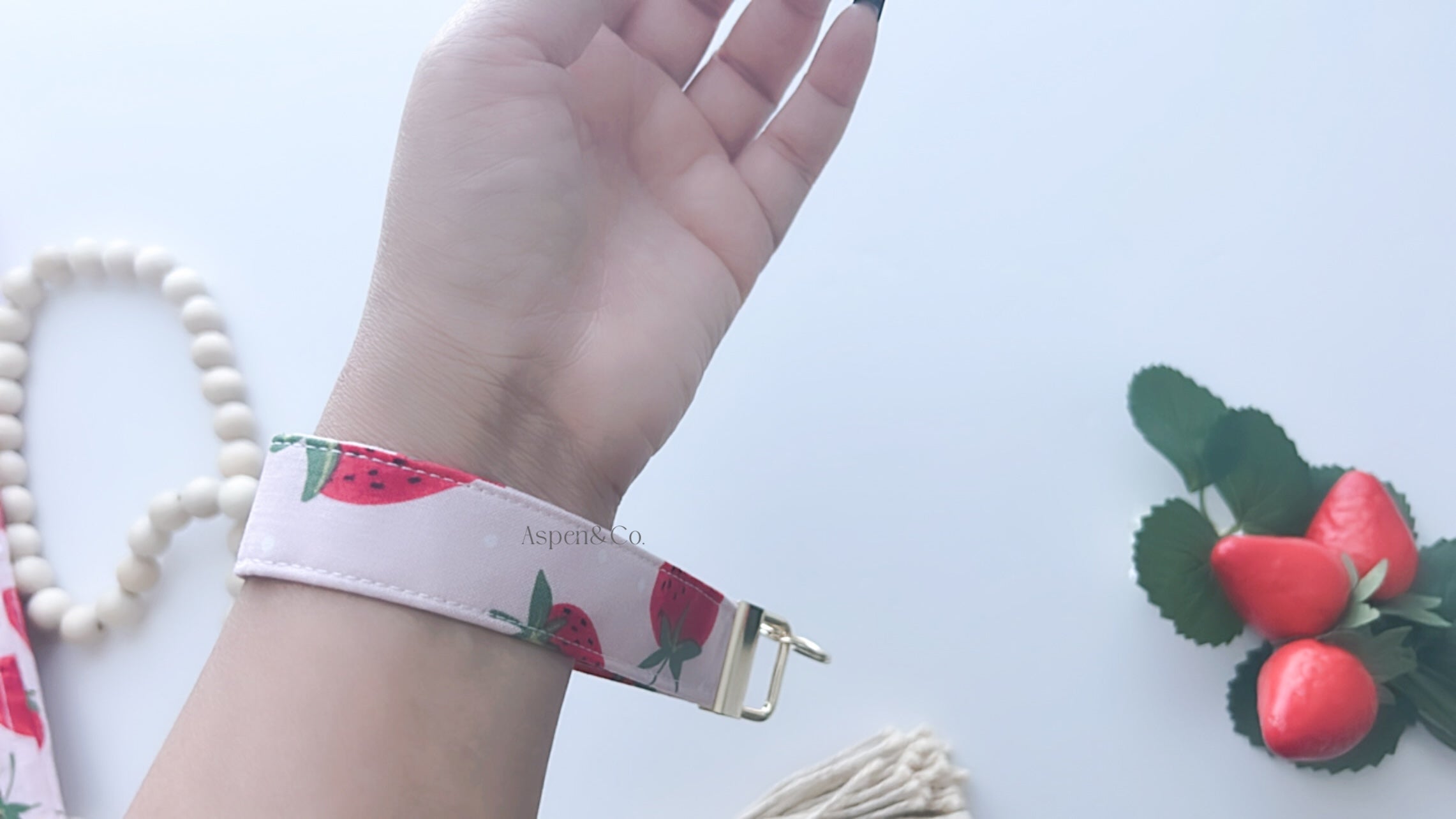 Hand wearing a floral keychain wristlet with decorative elements on a light background