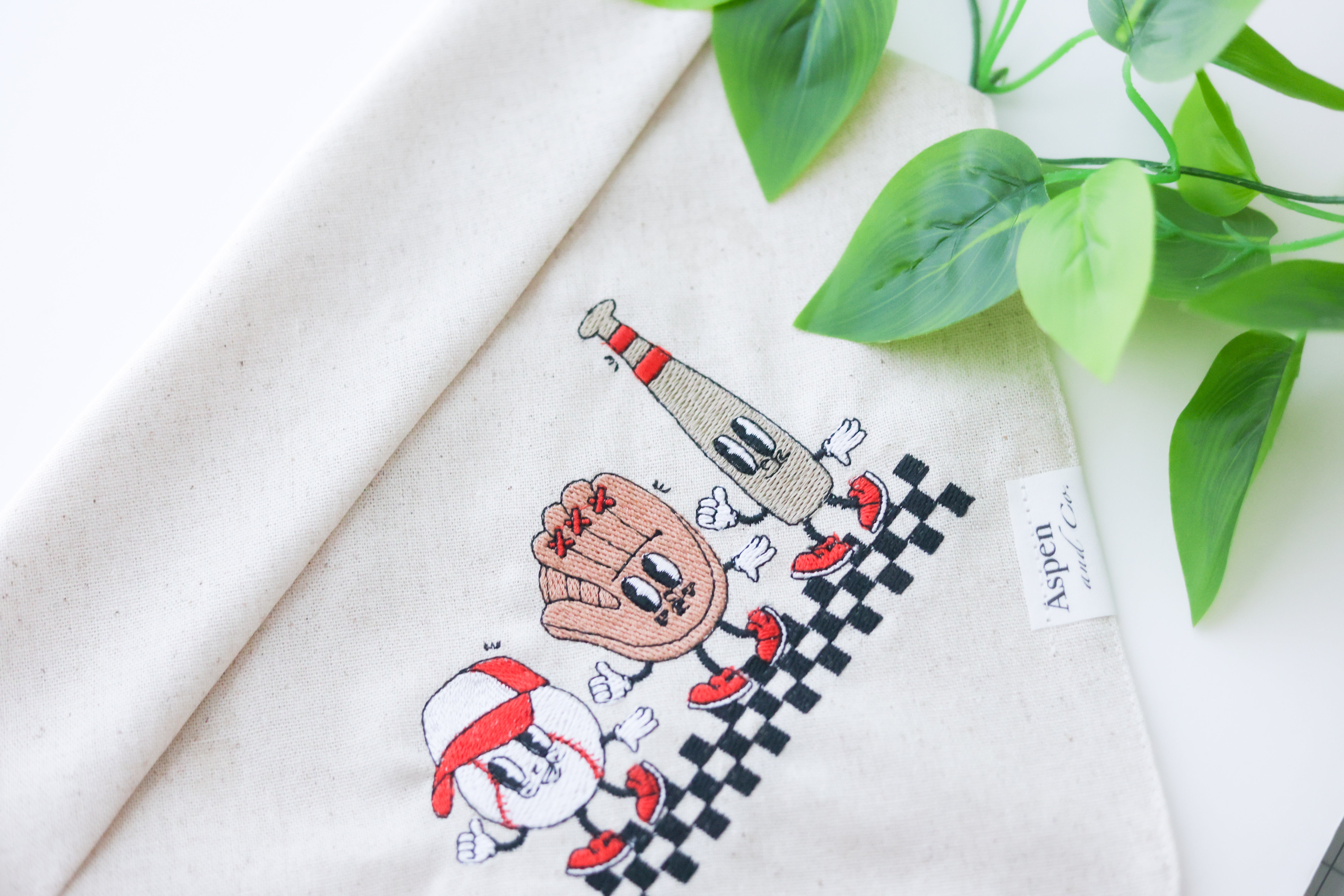 Linen dog bandana with embroidered smiley baseball, glove, and bat wearing a cap – sporty design perfect for baseball-loving pups.