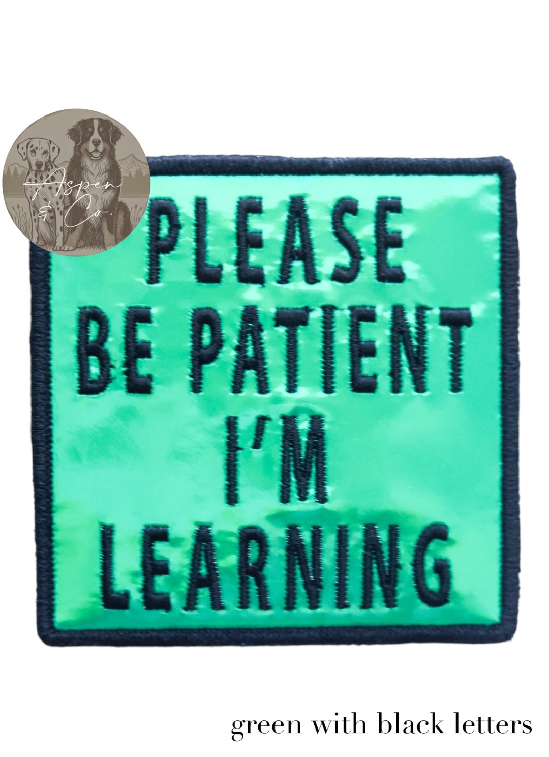 Green holographic embroidered dog patch with black text reading 'Please Be Patient I'm Learning,' shown close-up highlighting reflective finish and stitching. Suitable for attaching to dog harnesses, capes, or vests.