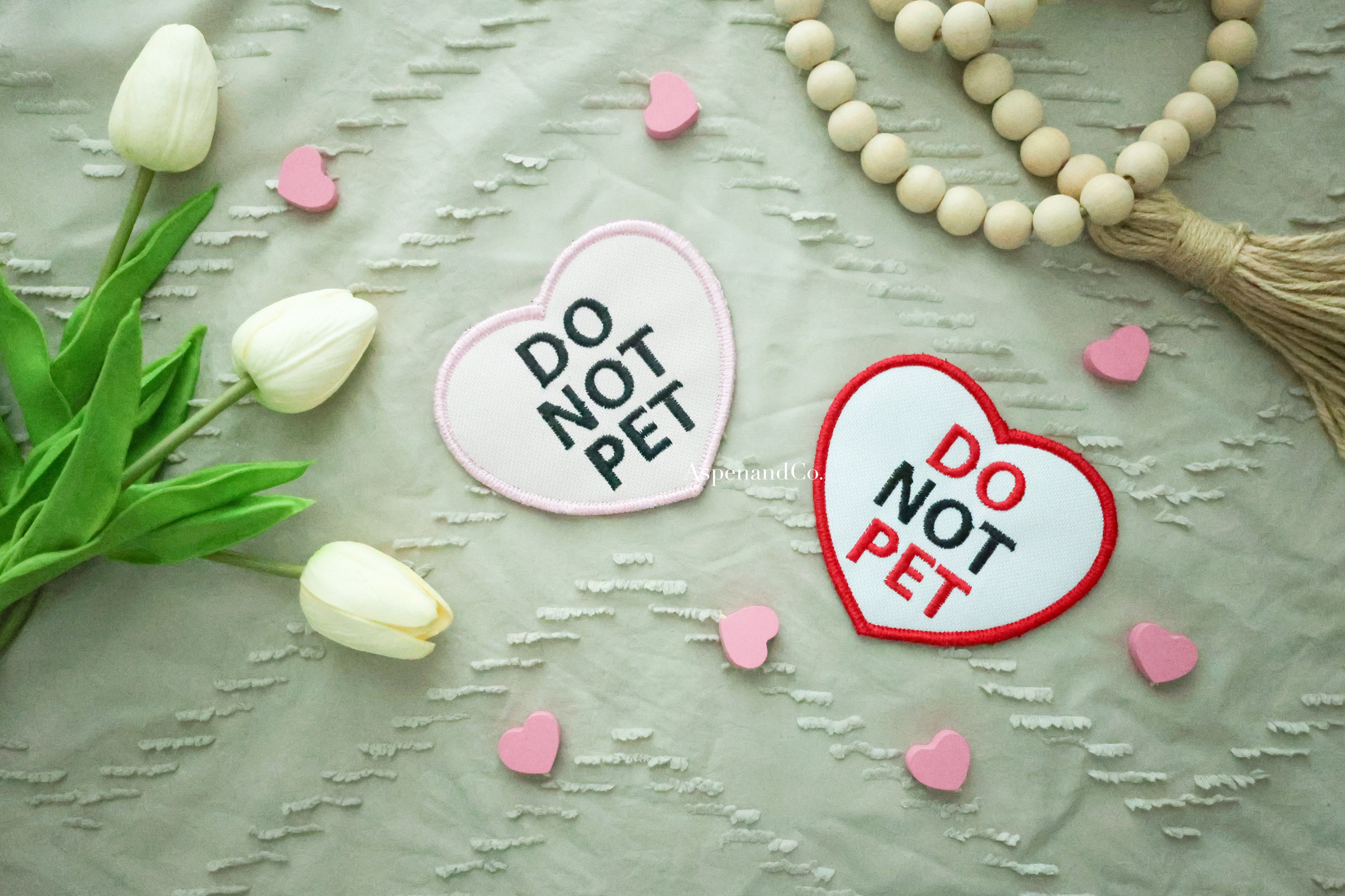 Side-by-side pink and white embroidered heart patches with 'DO NOT PET' text, designed for dog gear visibility