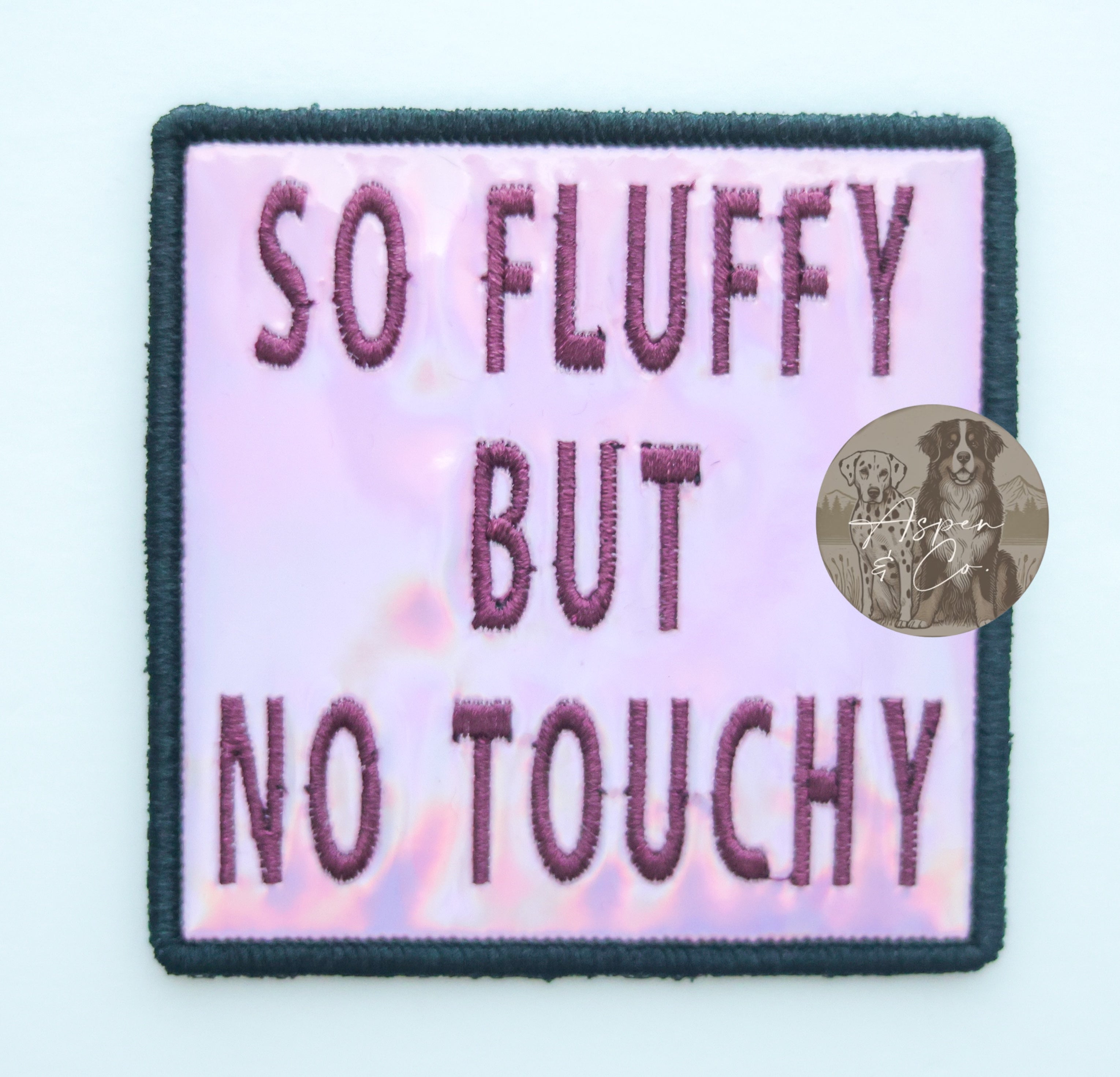 Pink holographic embroidered dog patch with plum 'So Fluffy But No Touchy' text, designed for attaching to dog vests, harnesses, or capes.