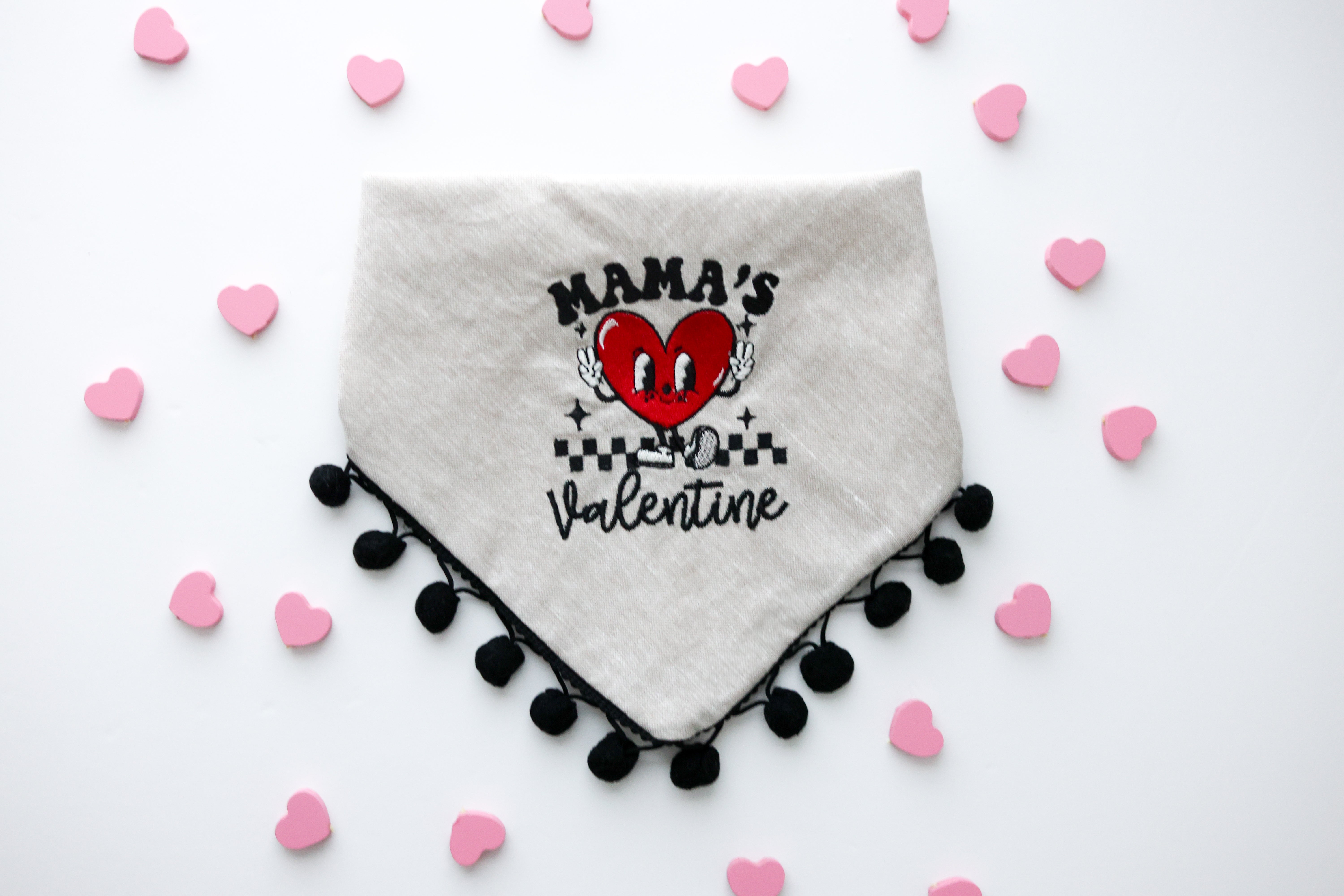 Tan linen dog bandana embroidered with a smiling heart character holding up peace fingers and wearing shoes.