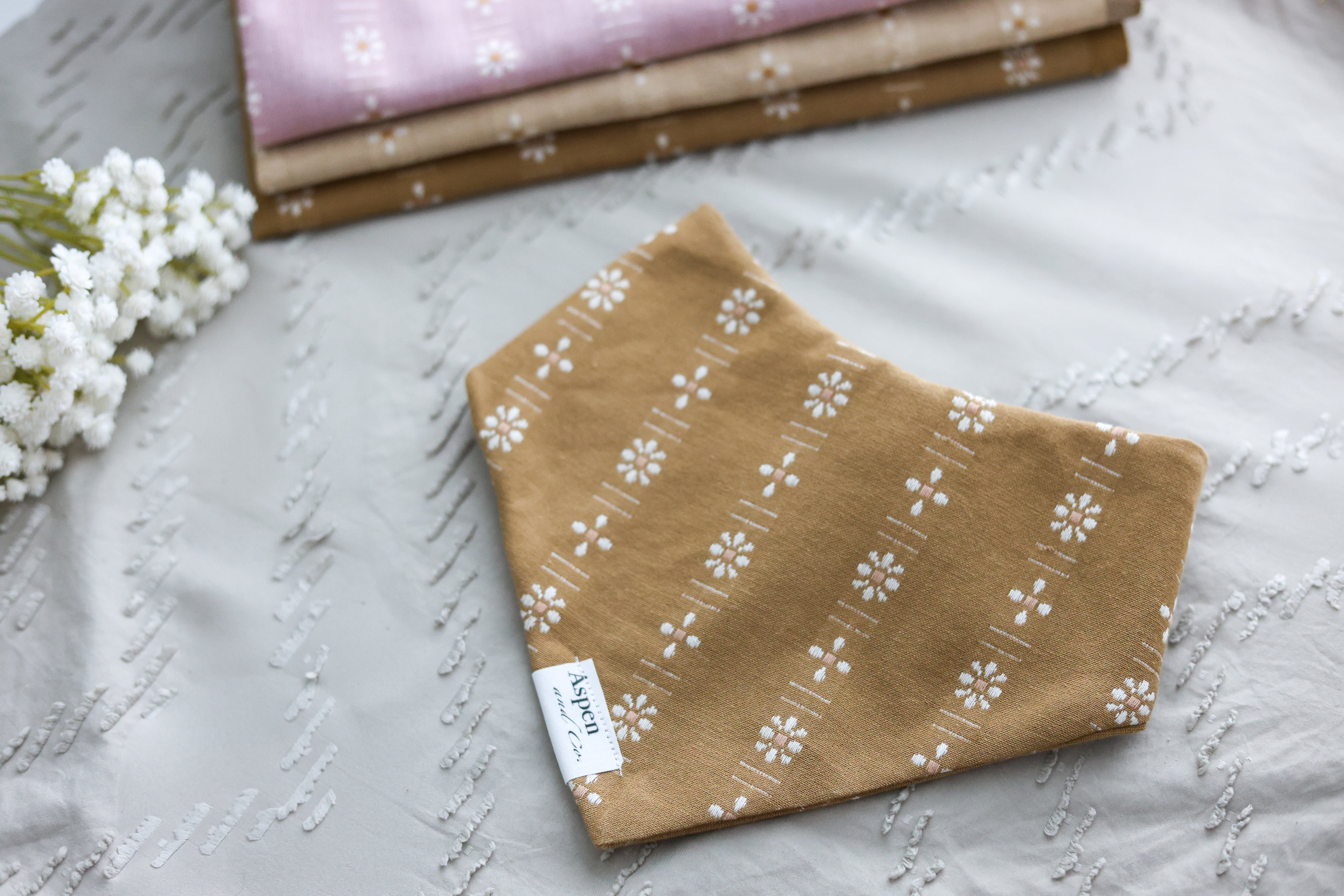 Front view of the Ochre floral slip-on dog bandana on a neutral sandy background.