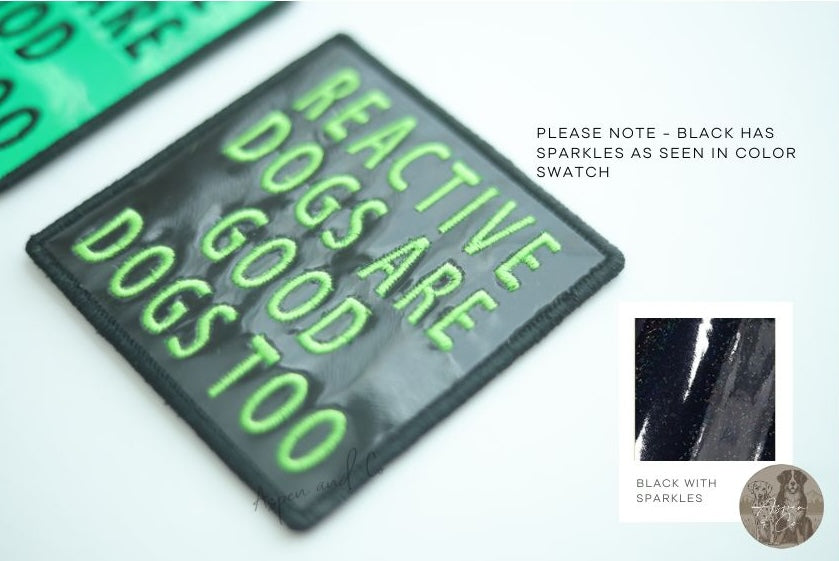 Close-up photo of a black holographic dog patch with neon green text reading "Reactive Dogs Are Good Dogs Too," designed for harnesses, vests, or capes.