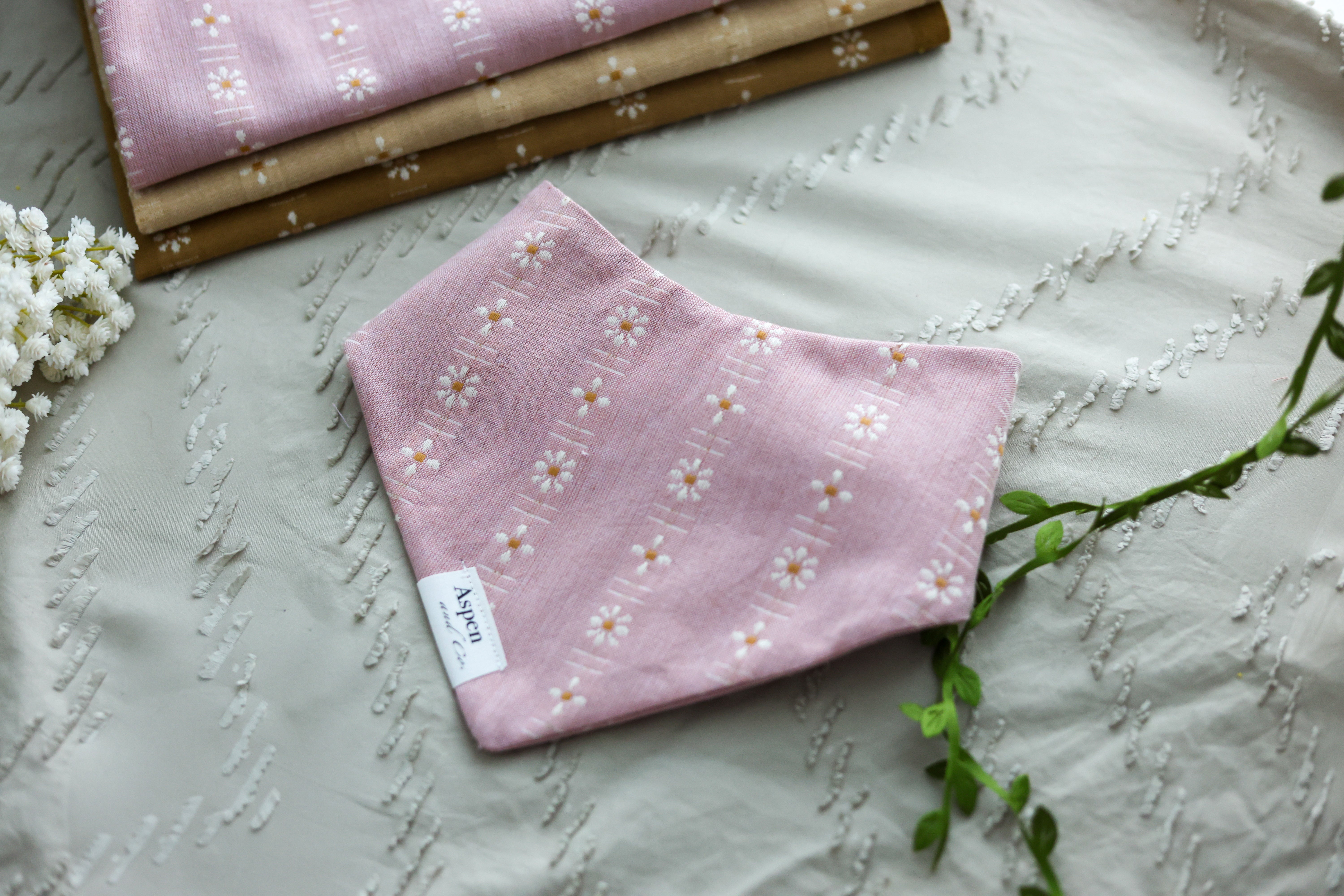 Front view of the Tea Rose Pink floral slip-on dog bandana on a neutral sandy background.